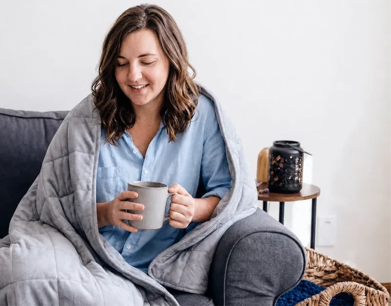 Woman relaxing at home under the Velin Weighted Blanket with a hot drink